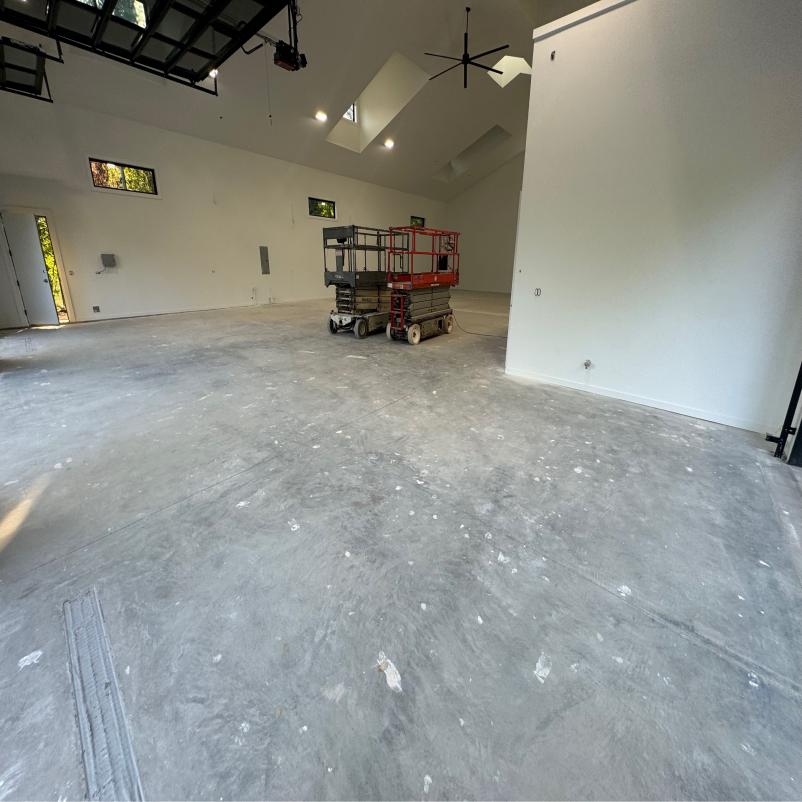 Spacious, unfinished interior with concrete floor, skylights, and two scissor lifts. Minimalist design and high ceiling contribute to an open, airy atmosphere.