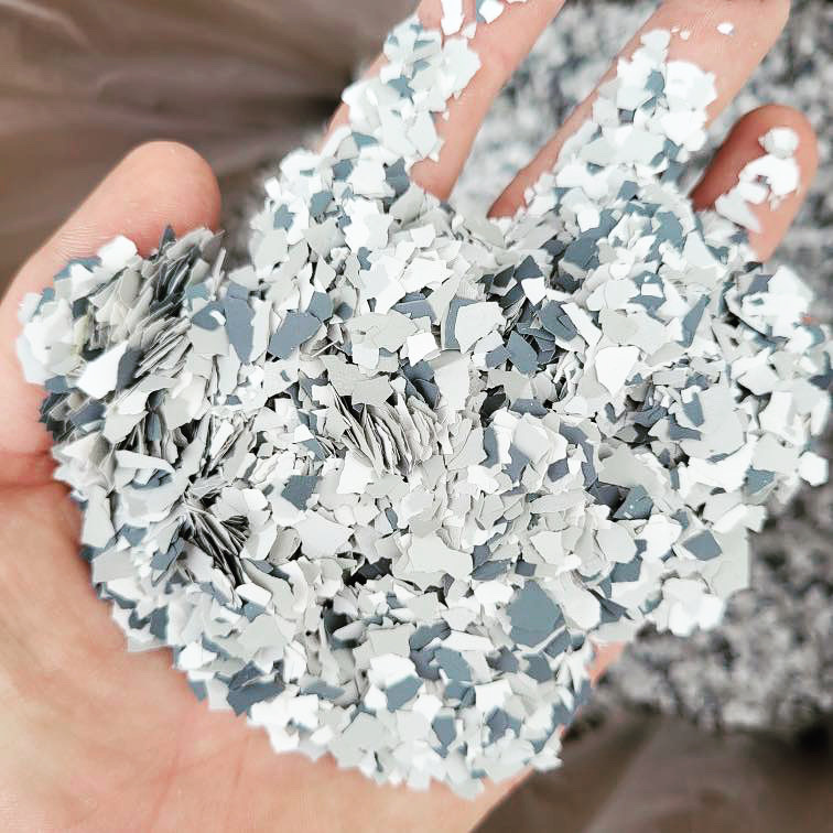 A person holds a handful of small, shredded plastic pieces in white, grey, and blue tones, creating a textured and layered appearance.