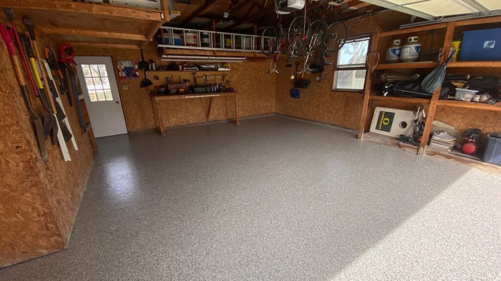 A tidy garage contains organized tools, bicycles, shelves, and a workbench with wood panel walls, a closed door, and a window.