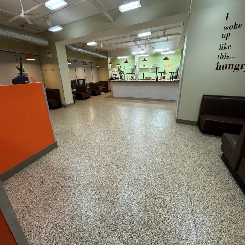 Bright café interior with orange accents, empty brown booths, white wall quote, and a counter. Modern lighting and sleek design create a welcoming atmosphere.